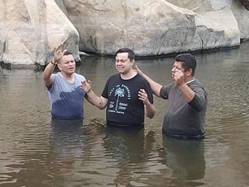 Personas de pie en un río durante un bautismo.