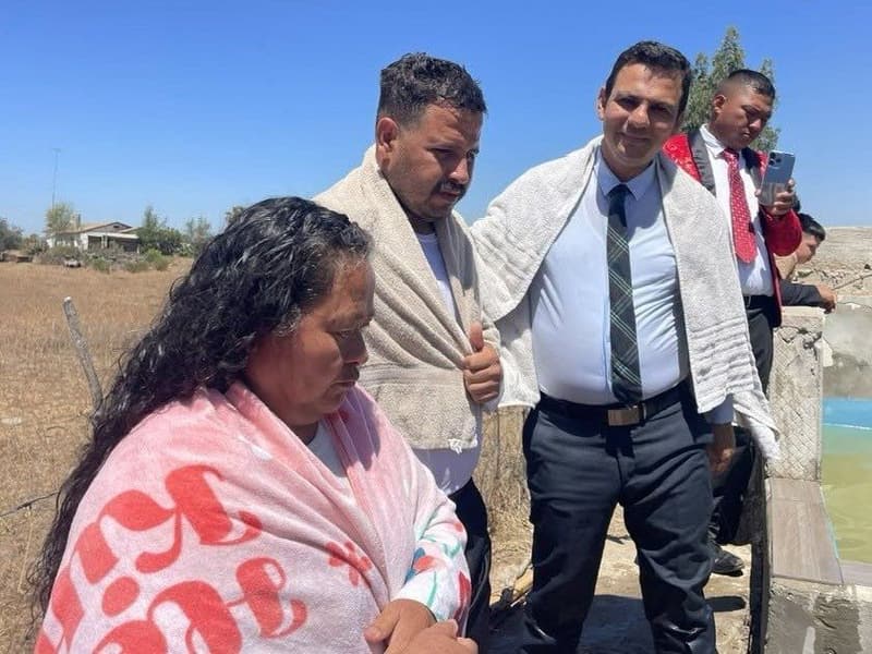 Una mujer y un hombre envueltos en toallas después del bautismo, con un pastor a su lado.