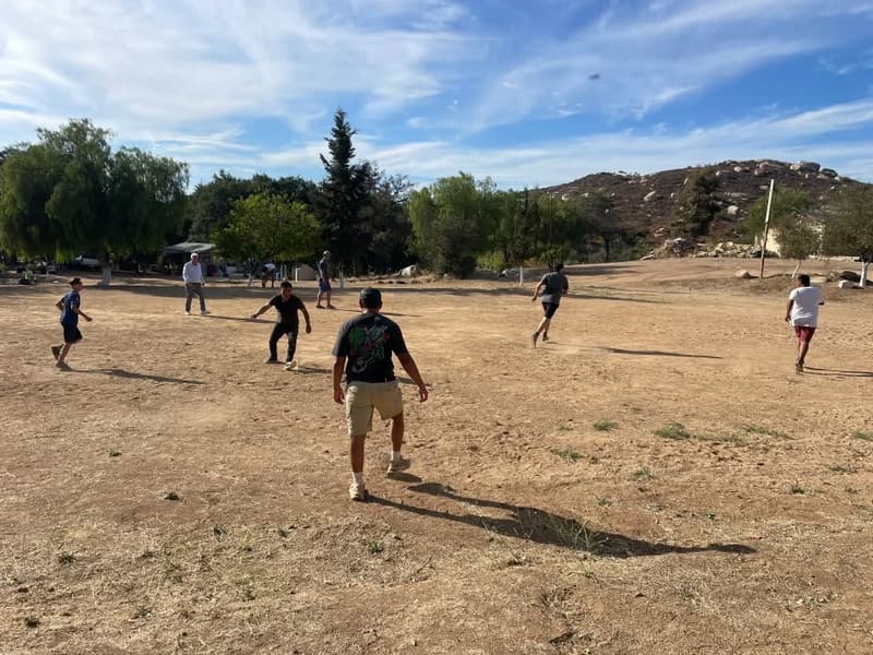 People playing soccer in an open field with hills behind, during the annual camp.