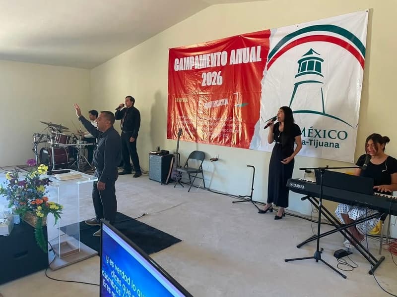 Worship at the annual camp: a woman sings at a microphone, with musicians at the drums and keyboard under the camp banner.
