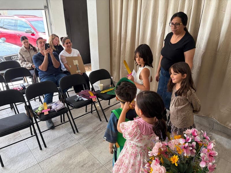 A teacher standing with children who hold paper swords, with flowers on the pulpit in front.