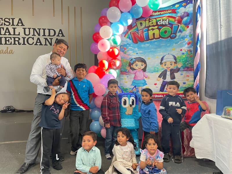 Children and a man holding a toddler in front of a Children's Day backdrop at the Ensenada church.