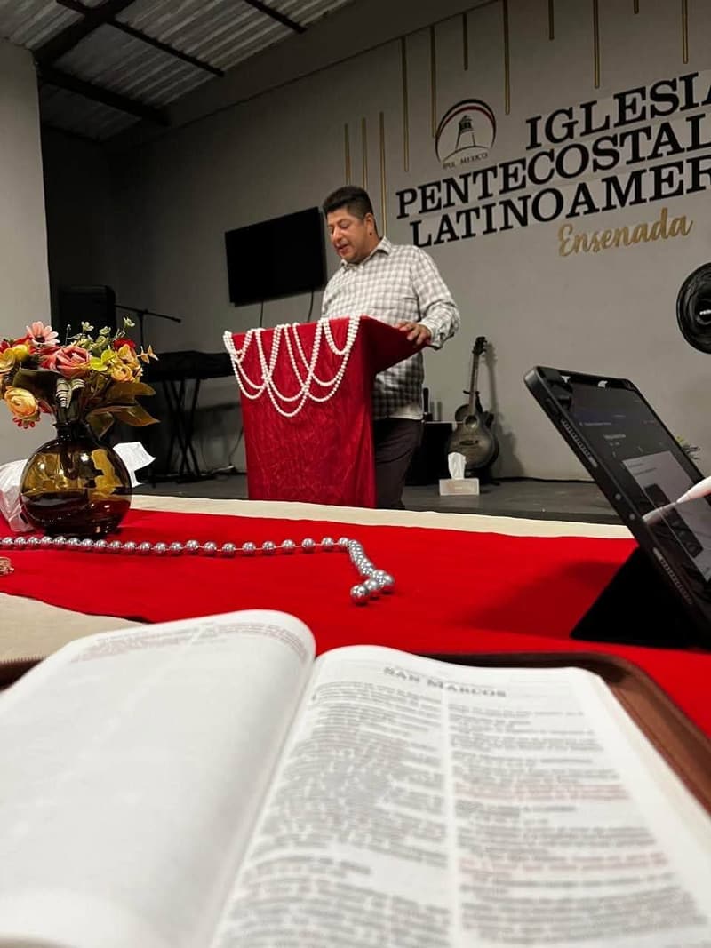Una Biblia abierta en primer plano y un hombre hablando en un púlpito en la iglesia de Ensenada.