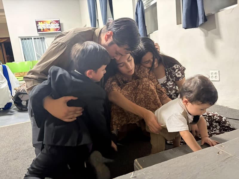 A man, two women and two small children praying together in an embrace at the front of a church.