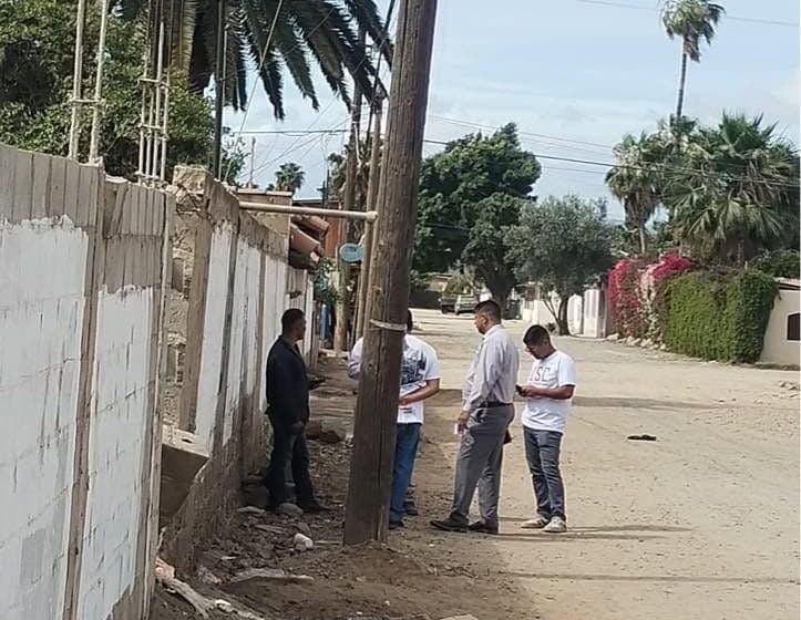 Church members talking with people on a dirt street in a neighborhood, beside a block wall.