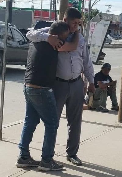 A church member embraces a man and prays with him on a city sidewalk.